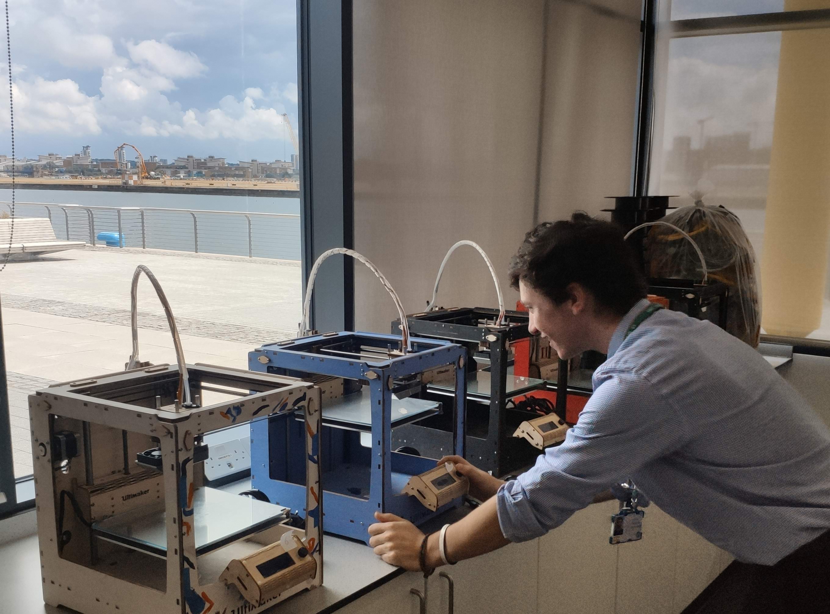 Myself leaning over a bank of Ultimaker 3D printers, printing visors for the NHS during the pandemic